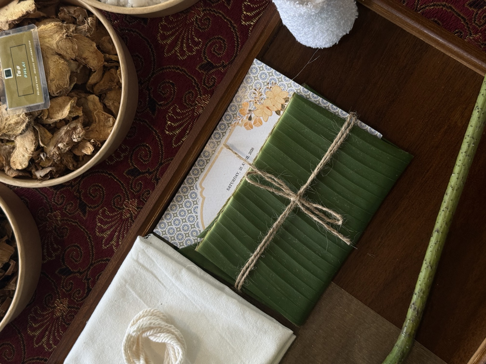 Banana-leaf wrapped workshop kit beside bowls of dried Thai herbs